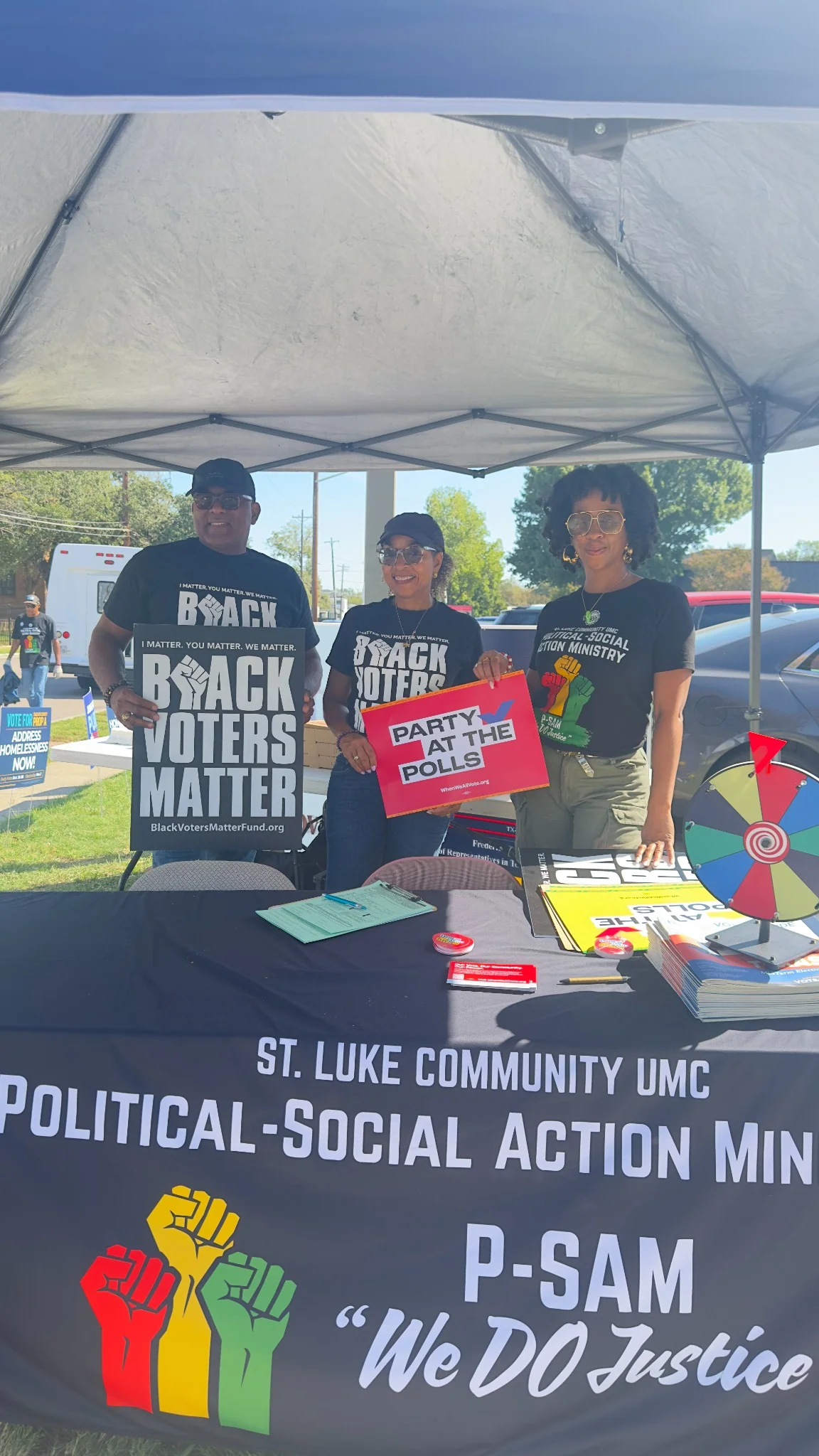 Three St. Luke P-SAM volunteers at a community voting event holding Party at the Polls and Black Voters Matter signs